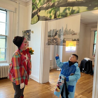 An NYC Bird Alliance volunteer engages with a young Island visitor below the work of 2023 AiR Carolyn Monastra.